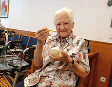 Ältere Frau hält lachend einen Eisbecher mit Waffel und Löffel in der Hand