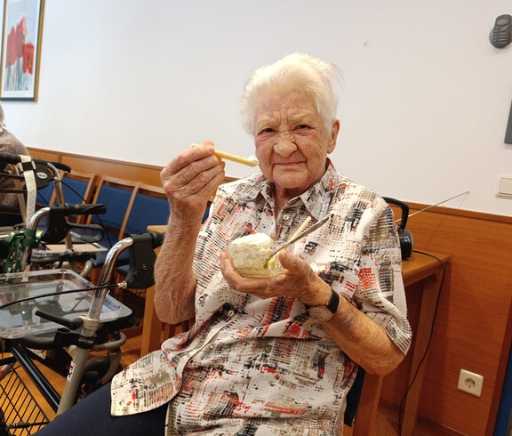 Ältere Frau hält lachend einen Eisbecher mit Waffel und Löffel in der Hand