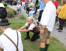 Mehrere Mitglieder der Pischelsdorfer Schuhplattler in Tracht demonstrieren das traditionelle Umlegen des Maibaums, während Bewohnerinnen und Bewohner des Caritas Pflegewohnhauses das Geschehen aus nächster Nähe verfolgen.
