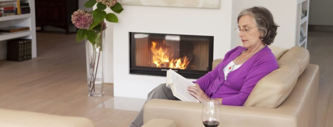Frau sitzt auf Sofa mit Caritas Notrufuhr und liest ein Buch