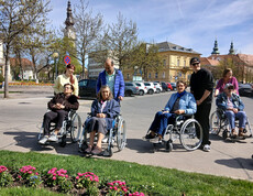 Gruppe von Menschen im Rollstuhl und Begleitpersonen macht Halt an einem Platz mit Frühlingsblumen in Klagenfurt.