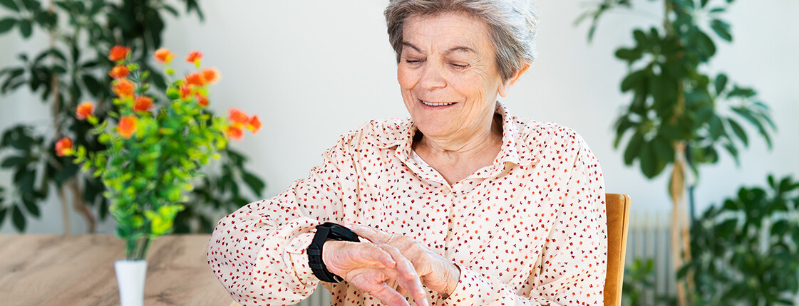 Ältere Frau zeigt auf Caritas Notrufuhr