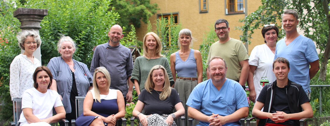 Gruppenfoto mehrerer Personen im Freien. 1. Reihe sitzt auf Stühlen, 2. Reihe steht.