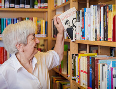 Eine Dame lächelt und zieht ein Buch aus einem Bücherregal.