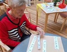 Eine Bewohnerin des Pflegewohnhauses nimmt im Rahmen des Tags der Demenz an einer Gedächtnisübung teil und ordnet Wortkarten an einem Tisch zu, während im Hintergrund weitere Mitmachstationen zu sehen sind.
