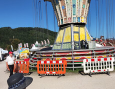 Buntes Kettenkarussell mit Absperrgittern, Marktstände und Wald im Hintergrund