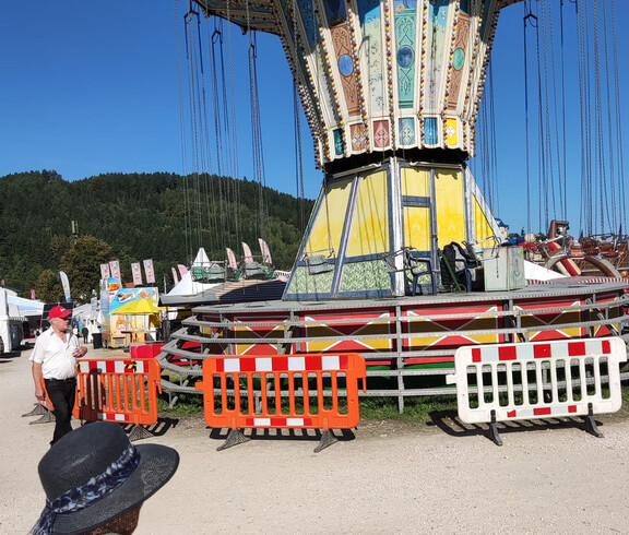 Buntes Kettenkarussell mit Absperrgittern, Marktstände und Wald im Hintergrund