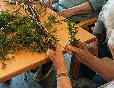 Bewohnerinnen des Pflegewohnhauses gestalten gemeinsam Palmbuschen. Auf dem Tisch liegen frische Zweige und Weidenkätzchen, während sorgfältig gebunden und gearbeitet wird