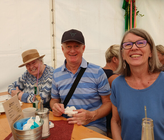 Bewohner*innen und Begleitpersonen sitzen gemeinsam an einem Tisch im Festzelt.