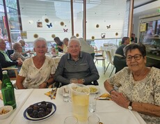 Beim Sommerfest im Pflegewohnhaus sitzen mehrere Bewohnerinnen und Bewohner gemeinsam an festlich gedeckten Tischen, während Speisen, Getränke und sommerliche Dekorationen für eine gesellige Atmosphäre sorgen.