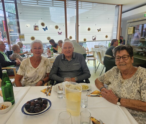 Beim Sommerfest im Pflegewohnhaus sitzen mehrere Bewohnerinnen und Bewohner gemeinsam an festlich gedeckten Tischen, während Speisen, Getränke und sommerliche Dekorationen für eine gesellige Atmosphäre sorgen.