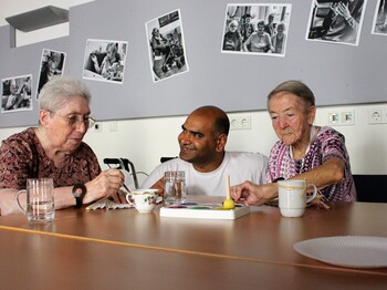 Zwei Seniorinnen sitzen am Tisch und malen, Pfleger in der Mitte