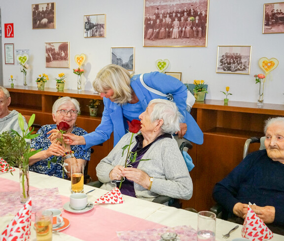 Zum Muttertag bekamen die Bewohnerinnen Rosen in einem festlich dekorierten Raum verteilt. Die Damen lächeln und genießen die herzliche Geste.