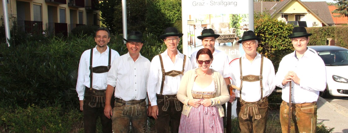 Sechs Mitglieder der Pischelsdorfer Schuhplattler posieren in traditioneller Tracht gemeinsam mit der Pflegedienstleitung vor dem Caritas Pflegewohnhaus Graz-Straßgang im Rahmen des Herbstfestes.
