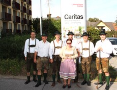 Sechs Mitglieder der Pischelsdorfer Schuhplattler posieren in traditioneller Tracht gemeinsam mit der Pflegedienstleitung vor dem Caritas Pflegewohnhaus Graz-Straßgang im Rahmen des Herbstfestes.