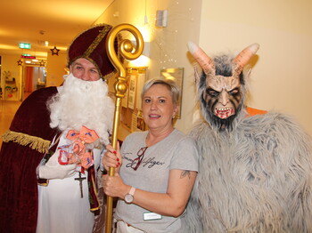 Nikolaus und Krampus posieren vor der Kamera, in der Mitte steht eine Pflegerin und hält den Stab des Nikolaus.