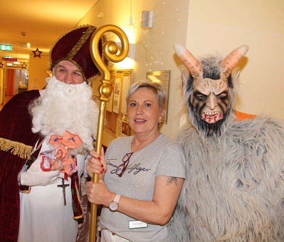 Nikolaus und Krampus posieren vor der Kamera, in der Mitte steht eine Pflegerin und hält den Stab des Nikolaus.