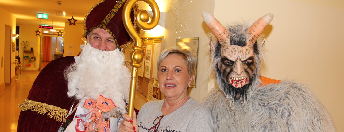 Nikolaus und Krampus posieren vor der Kamera, in der Mitte steht eine Pflegerin und hält den Stab des Nikolaus.