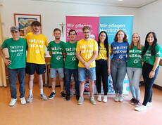 Zehn junge Erwachsene der Landjugend stehen mit bunten T-Shirts vor Caritas-Infobannern