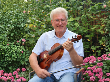 Mann sitzt, mit seiner Geige, im Garten