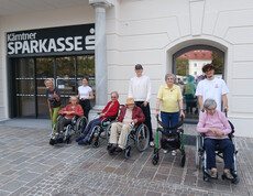 Gruppe von Senior*innen mit Begleitpersonen posiert vor dem Eingang der Kärntner Sparkasse.