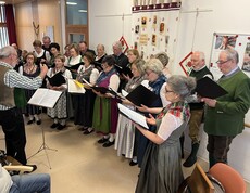 Ein Chor trägt Lieder im Gemeinschaftsraum eines Pflegewohnhauses vor, die Sängerinnen und Sänger halten Notenmappen