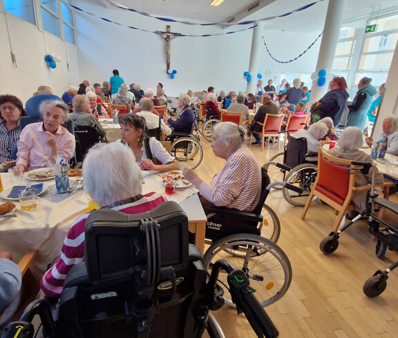 Viele Senior*innen sitzen an festlich gedeckten Tischen und genießen die Veranstaltung