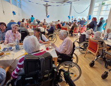Viele Senior*innen sitzen an festlich gedeckten Tischen und genießen die Veranstaltung