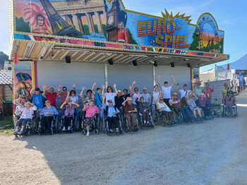Bewohner*innen und Begleitpersonen posieren vor einem Fahrgeschäft am Bleiburger Wiesenmarkt.