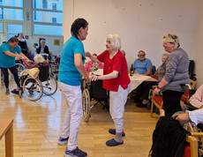 Senior*innen tanzen mit Pflegekräften, andere Gäste schauen lächelnd zu