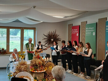 Zwei Geistliche feiern den Erntedank-Gottesdienst vor einer musizierenden Gruppe und herbstlichen Erntegaben.