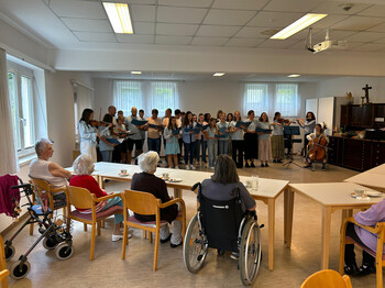 Schüler*innenchor mit Instrumentalist*innen singt Kirchen- und Kärntnerlieder vor Senior*innen im Pflegewohnhaus.