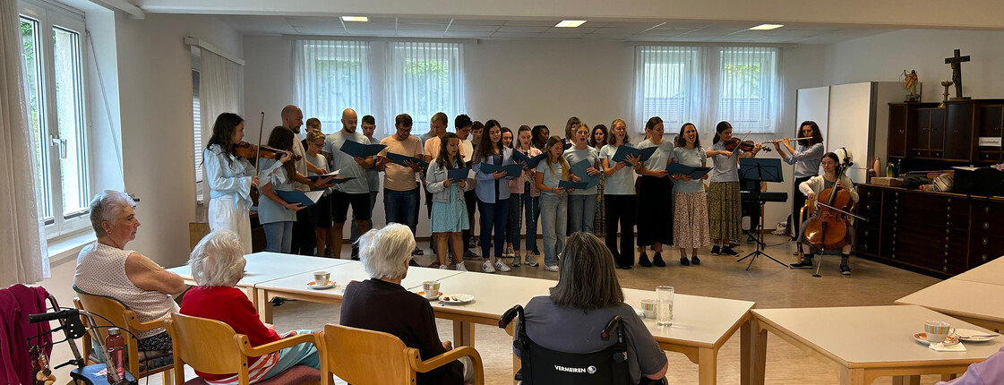 Schüler*innenchor mit Instrumentalist*innen singt Kirchen- und Kärntnerlieder vor Senior*innen im Pflegewohnhaus.