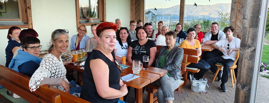 Mitarbeitende der PMS Group und Pflegekräfte vom Haus Elisabeth sitzen bei Getränken auf einer Terrasse mit Blick ins Tal.