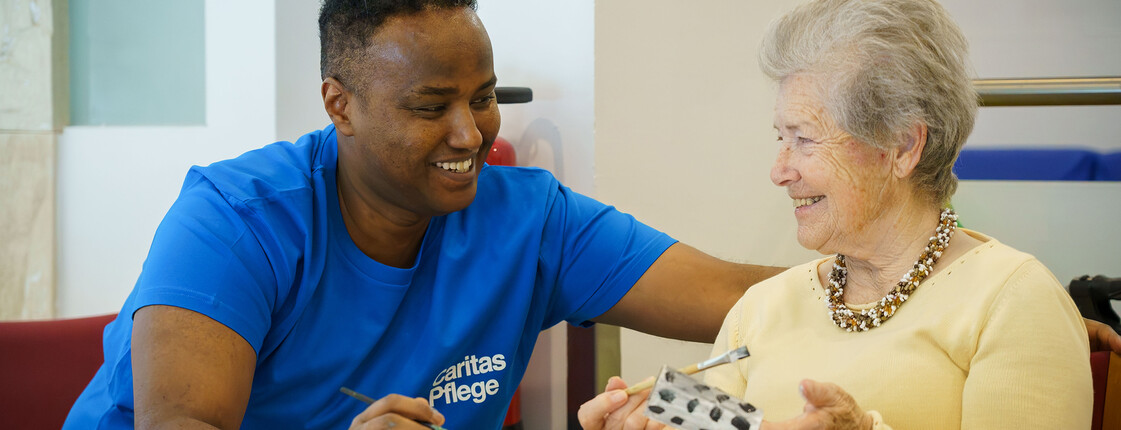 Pflegekraft unterstützt ältere Bewohner*in bei kreativer Beschäftigung im Pflegewohnhaus Haus Suavitas von Caritas.