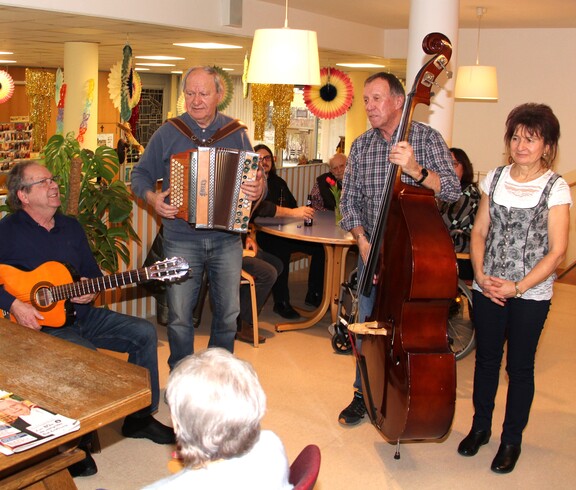 Eine Bewohnerin ist von hinten zu sehen, wie sie an ihrem Geburtstag den Musikanten zuhört. Die Musikanten stehen vor ihr und singen ein Lied zu ihren Ehren.