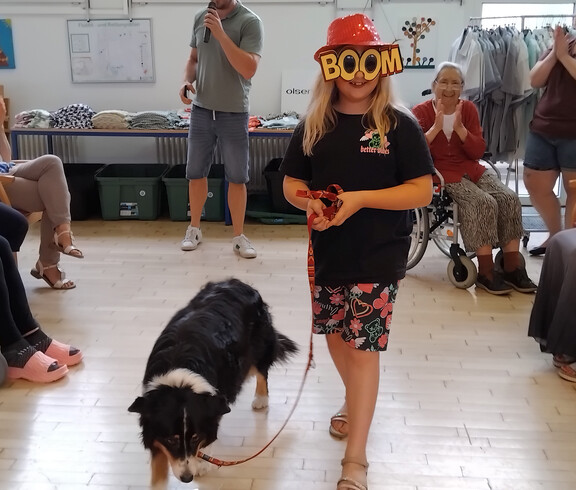 Kind mit auffälliger Brille führt Hund Emi über den Laufsteg, Publikum sitzt rundherum.