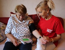 Caritas Mitarbeiterin der Hauskrankenpflege misst Blutdruck bei Klientin