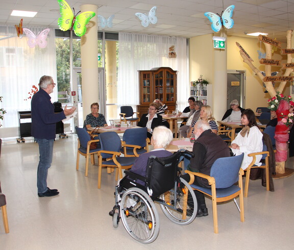 Dr. med. univ. Erwin Horst Pilgram hält im Pflegewohnhaus einen Impulsvortrag vor den anwesenden Angehörigen. Er steht im Vordergrund, spricht engagiert und vermittelt seine Inhalte mit fachlicher Kompetenz. Die Angehörigen hören aufmerksam zu.