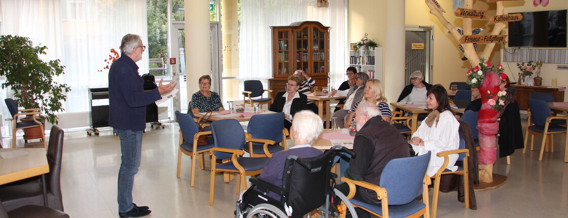 Dr. med. univ. Erwin Horst Pilgram hält im Pflegewohnhaus einen Impulsvortrag vor den anwesenden Angehörigen. Er steht im Vordergrund, spricht engagiert und vermittelt seine Inhalte mit fachlicher Kompetenz. Die Angehörigen hören aufmerksam zu.