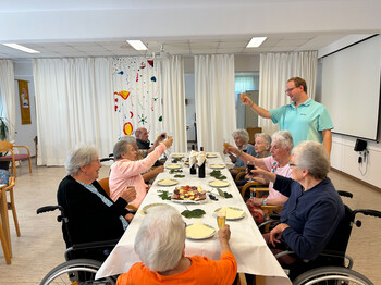 Bewohner*innen stoßen bei einer Weinverkostung im Festsaal des Hauses Franziskus gemeinsam an.