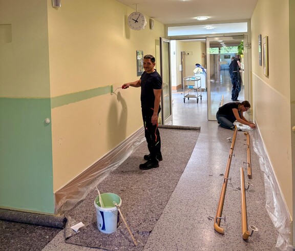Zu sehen ist ein Gang im Pflegewohnhaus. Auf einer Seite wurde der untere Wandbereich – wie ein Sockel – bereits von der Firma Fortna GmbH in Mintgrün ausgemalt. Die gegenüberliegende Seite wird noch abgeklebt und wartet auf den nächsten Arbeitsschritt.