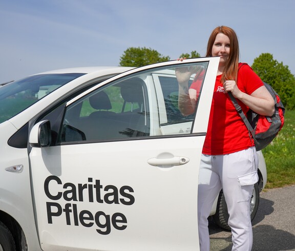 Eine Caritas Pflegerin neben einem Auto der mobilen Pflege.