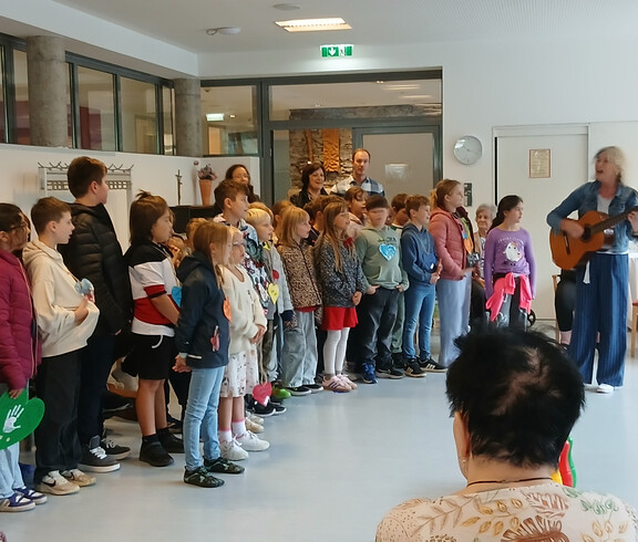 Schulklasse singt mit einer Lehrerin auf Gitarre für Senior*innen zum Tag der Sprachen.