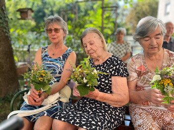 Drei ältere Frauen halten gesegnete Kräutersträuße auf dem Schoß im Garten