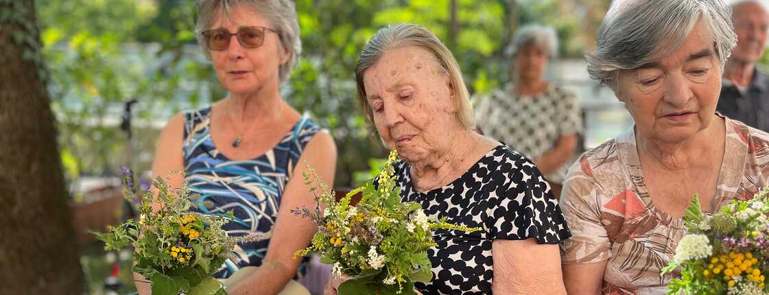 Drei ältere Frauen halten gesegnete Kräutersträuße auf dem Schoß im Garten