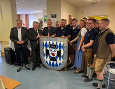 Der Veteranen- und Soldatenverein Alling zu Besuch im Pflegewohnhaus. Die Mitglieder, samt Hausleiter Josef Url, Bürgermeister Josef Niggas und Caritaspräsidentin und -direktorin Nora Tödtling-Musenbichler stehen in einer Gruppe, teilweise in Vereinskleidung. Im Hintergrund ist der Gemeinschaftsbereich des Hauses zu sehen.