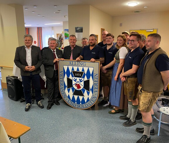 Der Veteranen- und Soldatenverein Alling zu Besuch im Pflegewohnhaus. Die Mitglieder, samt Hausleiter Josef Url, Bürgermeister Josef Niggas und Caritaspräsidentin und -direktorin Nora Tödtling-Musenbichler stehen in einer Gruppe, teilweise in Vereinskleidung. Im Hintergrund ist der Gemeinschaftsbereich des Hauses zu sehen.