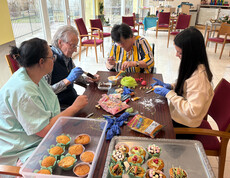 Bewohner*innen gestalten gemeinsam Osterdekoration und Süßspeisen an einem Tisch im Gemeinschaftsraum.