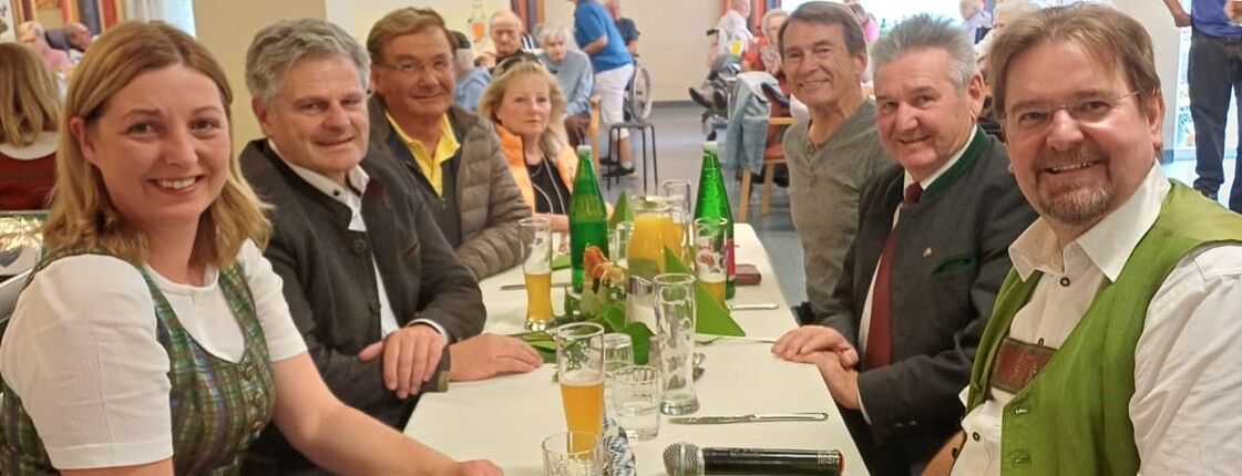 Im Gemeinschaftsraum sitzen die Gäste an einem gedeckten Tisch. Unter ihnen befinden sich Bürgermeister Josef Niggas, Caritaspräsidentin und -direktorin Nora Tödtling-Musenbichler sowie Max Tödtling, Moderator der Feier und ehemaliger Hausleiter. Im Hintergrund sind weitere Tische und der Raum sichtbar.